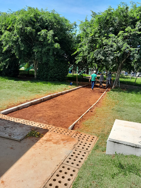 passarela de terra com três homens trabalhando na construção, ao fundo árvores e grama em ambos os lados da obra.
